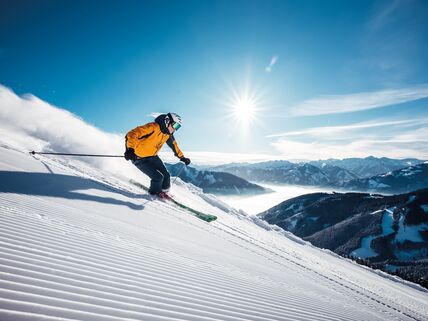 A skier in a yellow jacket glides down a freshly groomed slope.