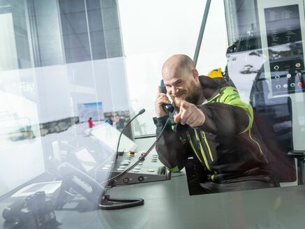 Mitarbeiter in einer Liftstation, der in einer Hand das Telefon hält und mit der anderen Hand auf den Betrachter zeigt. | © Max Steinbauer